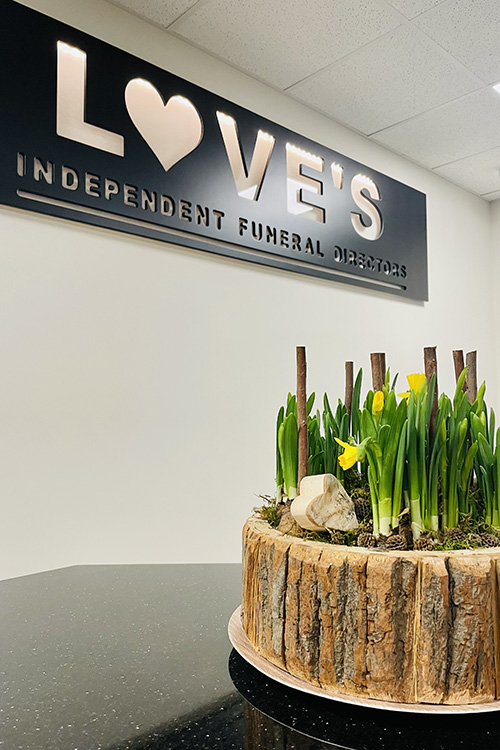 Love's Independent Funeral Directors sign underneath a tub of flowering daffodils